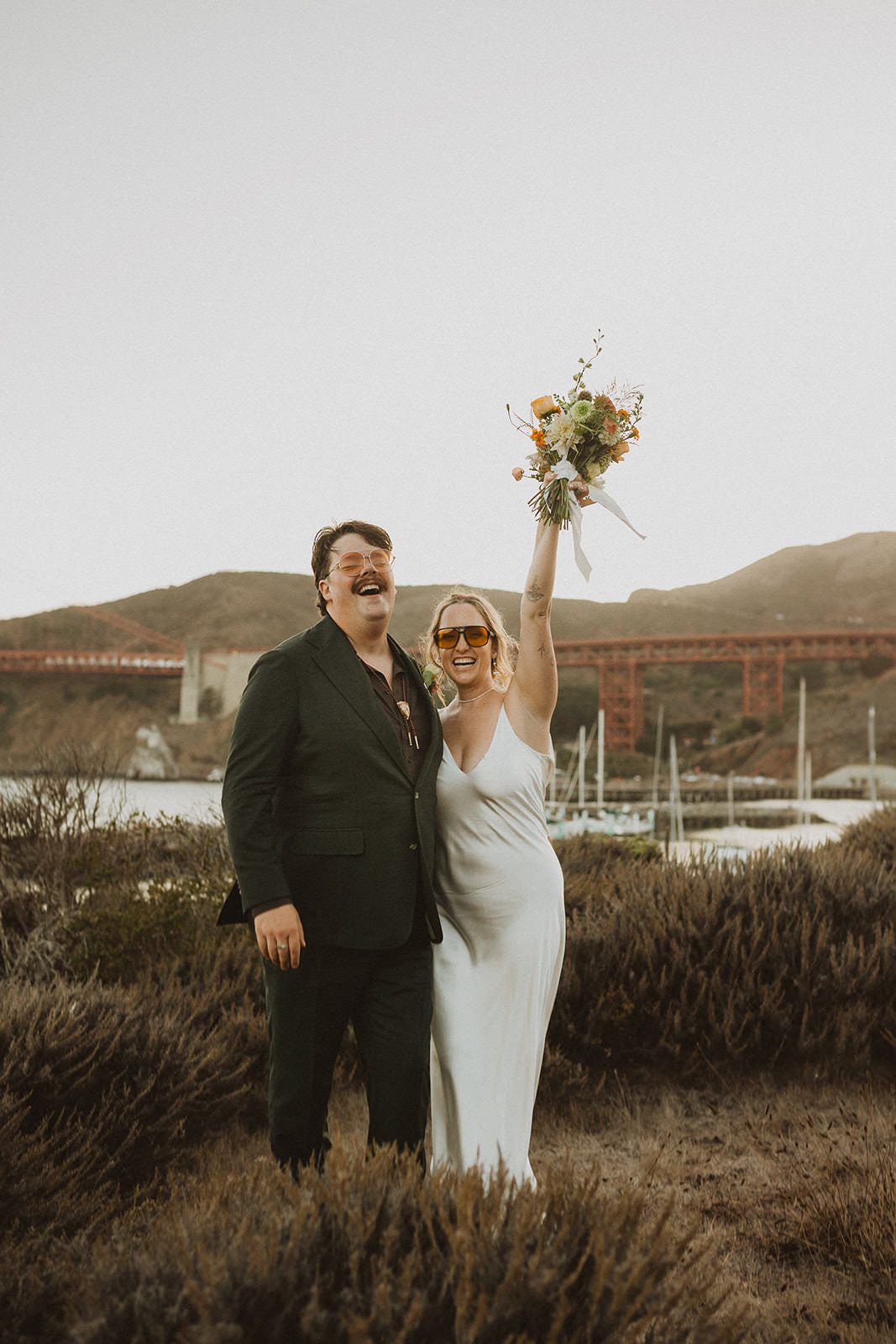 Bride and groom celebrating by the water with Golden Gate Bridge at Travis Marina wedding in Sausalito